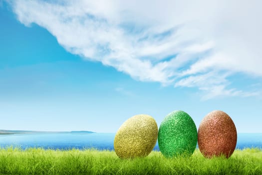 Colorful easter eggs on the green grass with blue ocean view and cloudscapes over blue sky background. Happy Easter