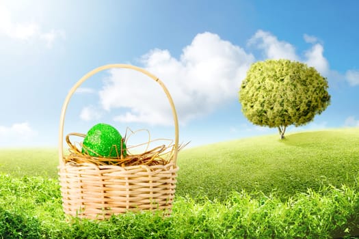 Green easter egg in the nest on wooden basket on the green grass with tree and blue sky background. Happy Easter