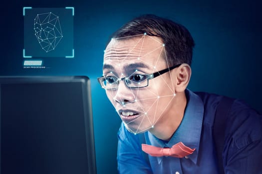 Attractive asian businessman with laptop using face recognition over blue background. Modern technology concept