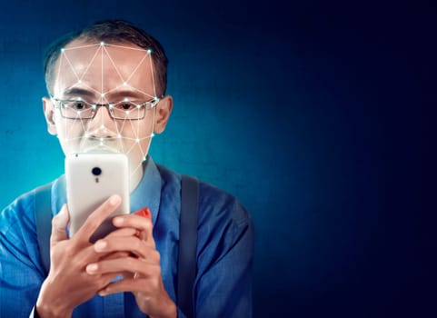 Attractive asian businessman with mobile phone using face recognition over blue background. Modern technology concept