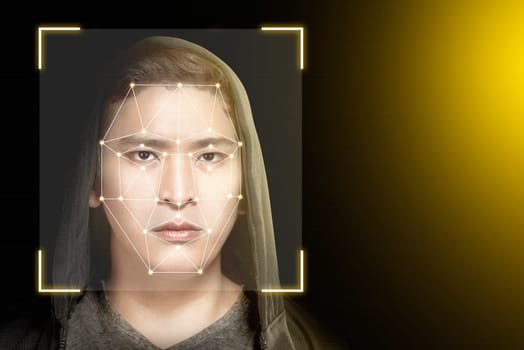 Young asian man in black hoodie using face recognition over dark background. Modern technology concept