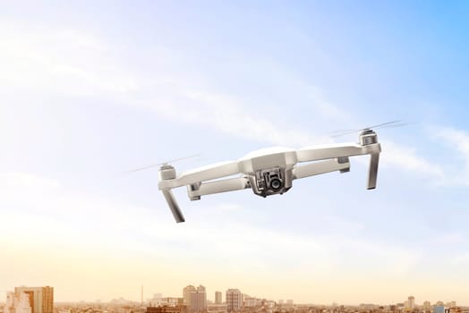 White drone with camera flying over the city with sunset view background