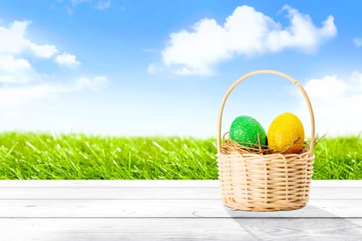 Colorful easter eggs in the nest on wooden basket on wooden table with grass field and blue sky background. Happy Easter
