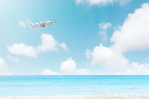 White drone with camera flying over the beach with blue ocean and blue sky background