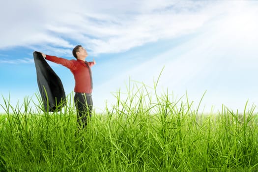 Happy asian businessman with open arms holding a suit standing on the grass with blue sky background