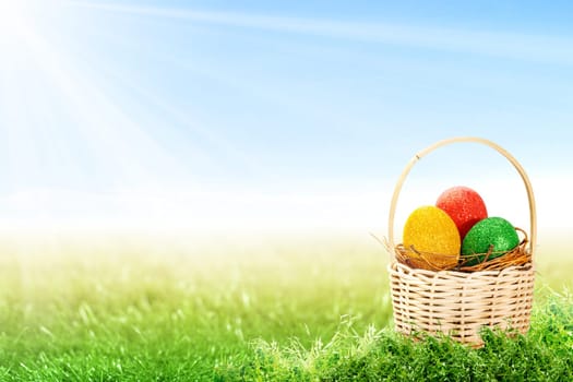 Colorful easter eggs in the nest on wooden basket on the grass field with sunlight and blue sky background. Happy Easter