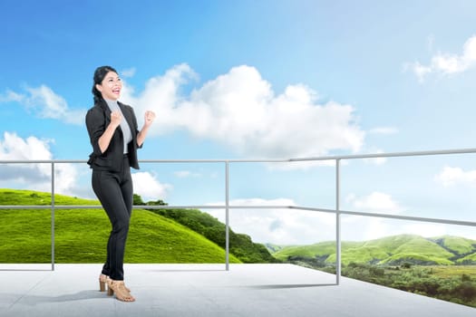 Excited asian business woman standing on the terrace with green landscapes view and blue sky background