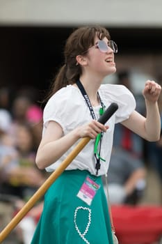 Louisville, Kentucky, USA - May 03, 2018: The Pegasus Parade, young woman carrying a  broom and wearing retro clothing, singing and dancing while going down w broadway