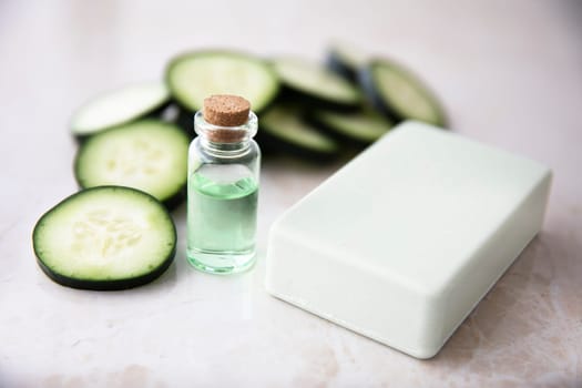 Cucumber extract in small bottle with bar of soap and cucumber slices.