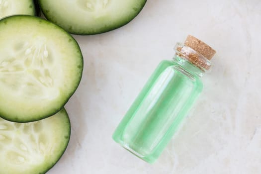 Cucumber slices and small bottle of cucumber extract flat lay.