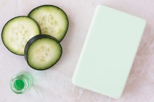 Cucumber extract in small bottle with bar of soap and cucumber slices flat lay