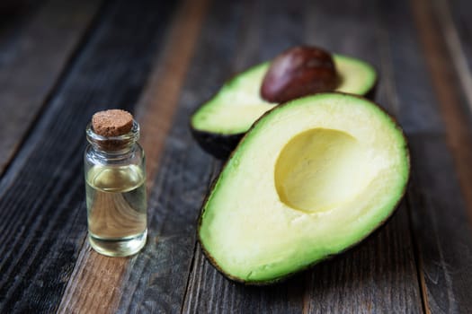 Small bottle of avocado oil and avocados on wooden table