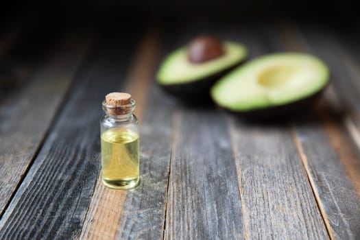 Small bottle of avocado oil and avocados on wooden table