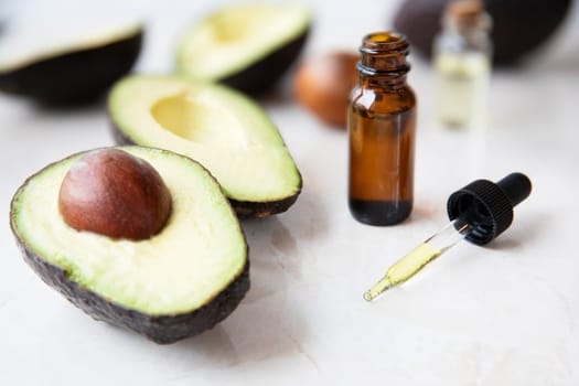 Small bottle with dropper of avocado oil and avocados on marble surface.