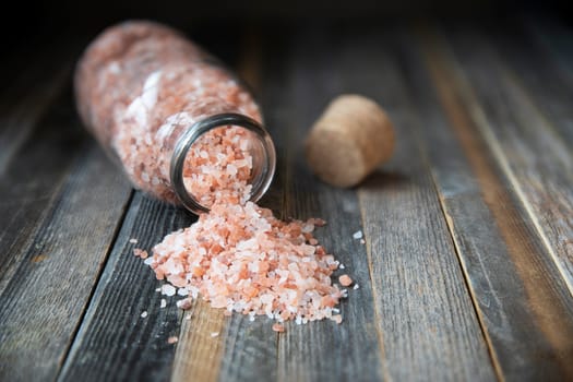 Pink Himalayan salt crystals in glass bottle and small bowl on wooden table.