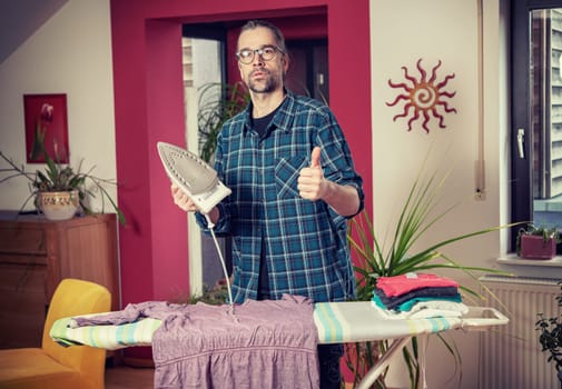 man with iron on ironing board with thumb up in living room