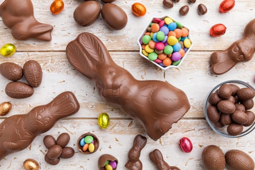 Delicious chocolate Easter bunny, eggs and sweets on rustic background