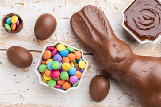 Delicious chocolate Easter bunny, eggs and sweets on rustic background