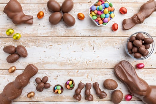 Delicious chocolate Easter bunny, eggs and sweets on rustic background