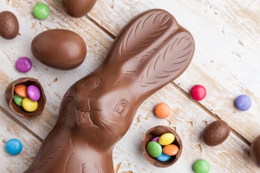 Delicious chocolate Easter bunny, eggs and sweets on rustic background