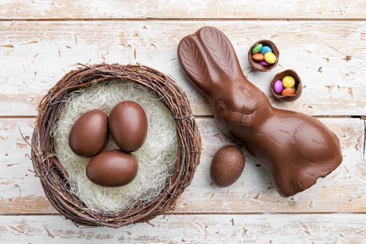 Delicious chocolate Easter bunny, eggs and sweets on rustic background
