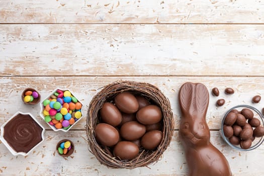 Delicious chocolate Easter bunny, eggs and sweets on rustic background