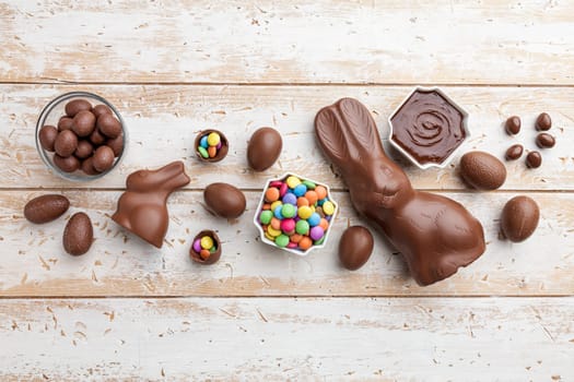 Delicious chocolate Easter bunny, eggs and sweets on rustic background