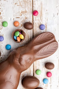 Delicious chocolate Easter bunny, eggs and sweets on rustic background