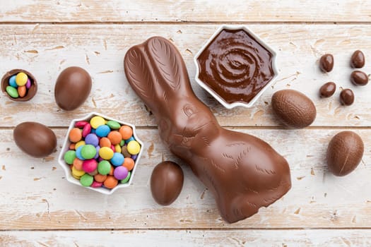 Delicious chocolate Easter bunny, eggs and sweets on rustic background
