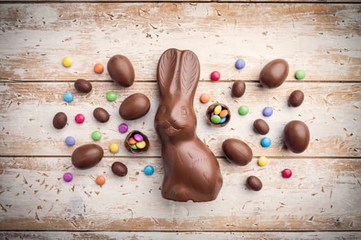 Delicious chocolate Easter bunny, eggs and sweets on rustic background