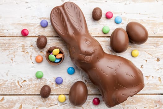 Delicious chocolate Easter bunny, eggs and sweets on rustic background