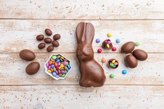 Delicious chocolate Easter bunny, eggs and sweets on rustic background