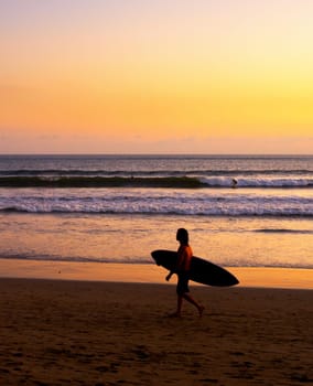 Surfer on beach at scenic sunset, Bali, Indonesia