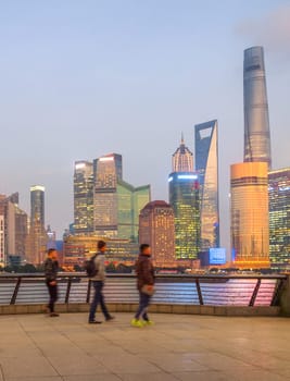 People walking at embankment enjoying illuminated evening Shanghai cityscape view, China