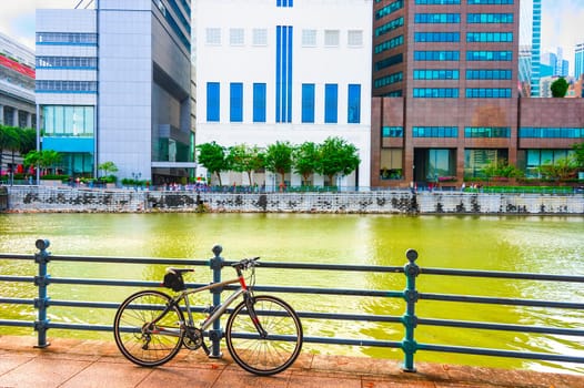 Bicycle parked at city quay by river, skyscrapers of modern architecture in background, Singapore