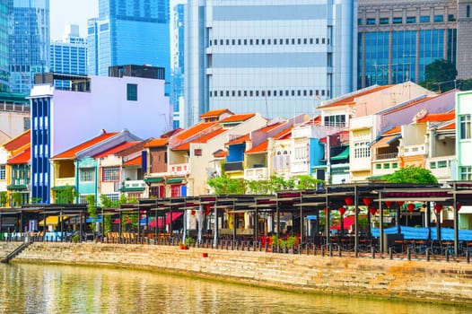 Cityscape with colorful bars, restaurants and stores by the Singapore River along Boat Quay, skyscrapers of modern architecture in background