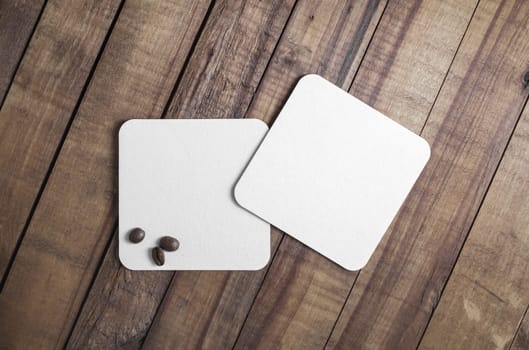 Two blank square beer coasters and coffee beans on wood table background. Flat lay.
