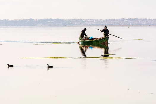 Bruncuteula, Sant'Antioco, Italy - January 28, 2016: Fishermen with their ancient boats, fall at dawn, landscape of the lagoon of Sant'Antioco in south west Sardinia.