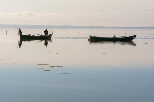 Bruncuteula, Sant'Antioco, Italy - January 28, 2016: Fishermen with their ancient boats, fall at dawn, landscape of the lagoon of Sant'Antioco in south west Sardinia.