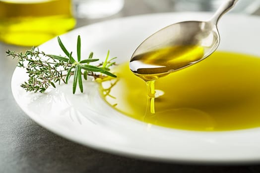 Healthy olive oil with herbs pouring with spoon close up