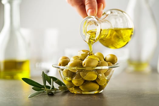 Organic olive oil. Bottle of Extra virgin oil pouring in to glass bowl with olives