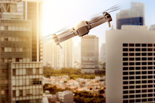 White drone with camera flying above modern city with skyscrapers and sunset view background