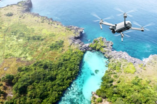 White drone with camera flying above the landscapes with green trees, blue lake and blue ocean on the daytime