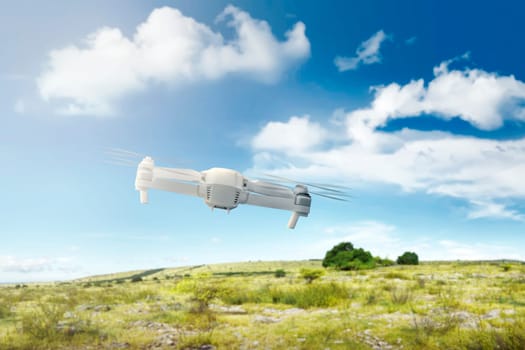 White drone with camera flying above the field with green grass and trees with blue sky background