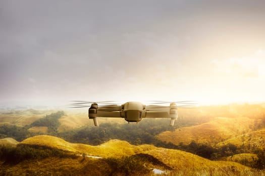 White drone with camera flying above green hills and trees with sunlight background