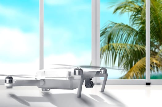 White drone with camera on white table with window glass and palm tree with blue sky background