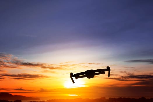 Silhouette of drone with camera flying over sunset view background