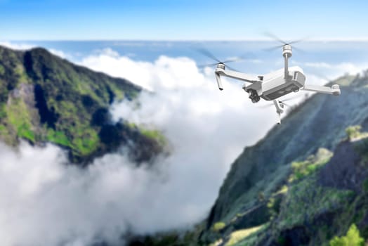 White drone with camera flying above the top of mountain with cloudscapes and blue sky background