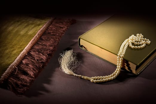Quran and prayer beads with prayer mat on the floor over black background
