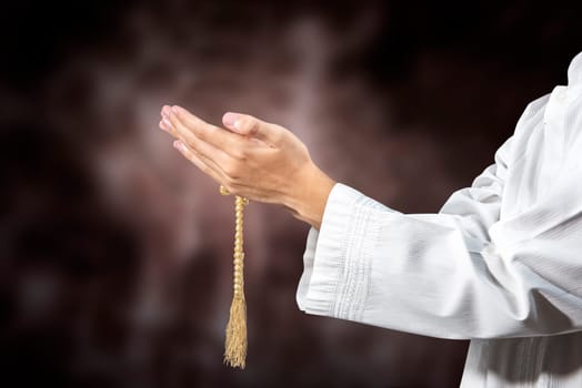 Muslim man praying with prayer beads on his hands over blurry background